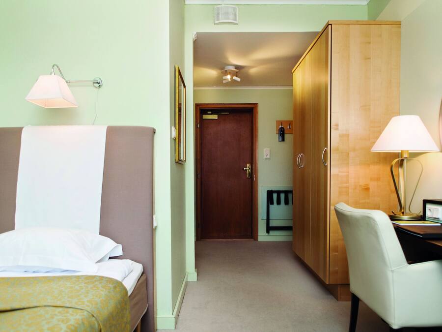 A hotel room with a bed, a desk, a chair, a wardrobe, and a bathroom door.