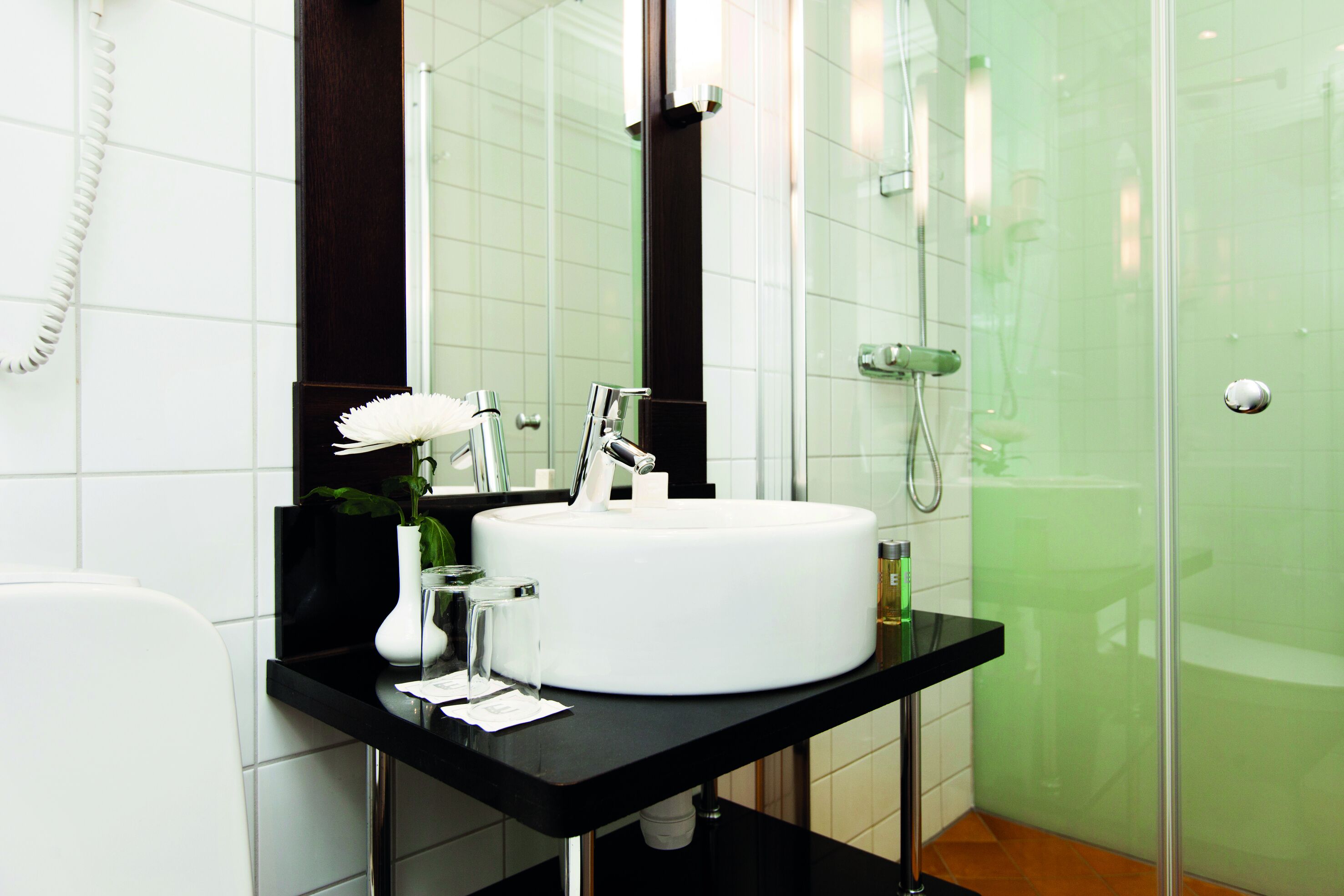 Un baño moderno con un lavabo blanco, un espejo, ducha y teléfono.