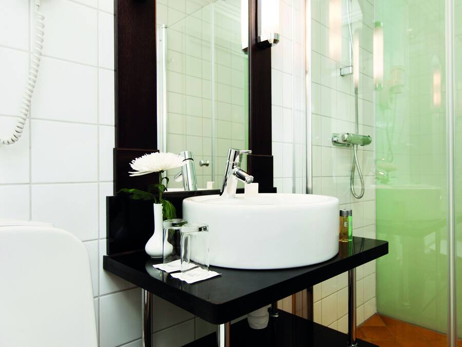 Un baño moderno con un lavabo blanco, un espejo, ducha y teléfono.