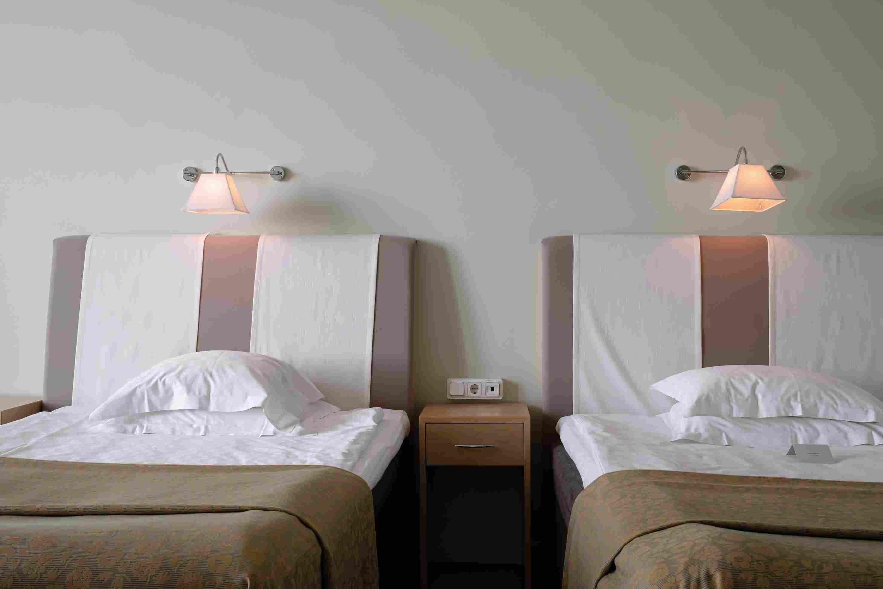 Two twin beds with headboards, a nightstand with a lamp, and a power outlet.