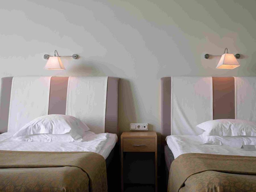 Two twin beds with headboards, a nightstand with a lamp, and a power outlet.
