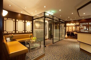 A lobby with a glass partition, a seating area with a table, and a reception desk. - Ambassador Hotel (Düsseldorf)