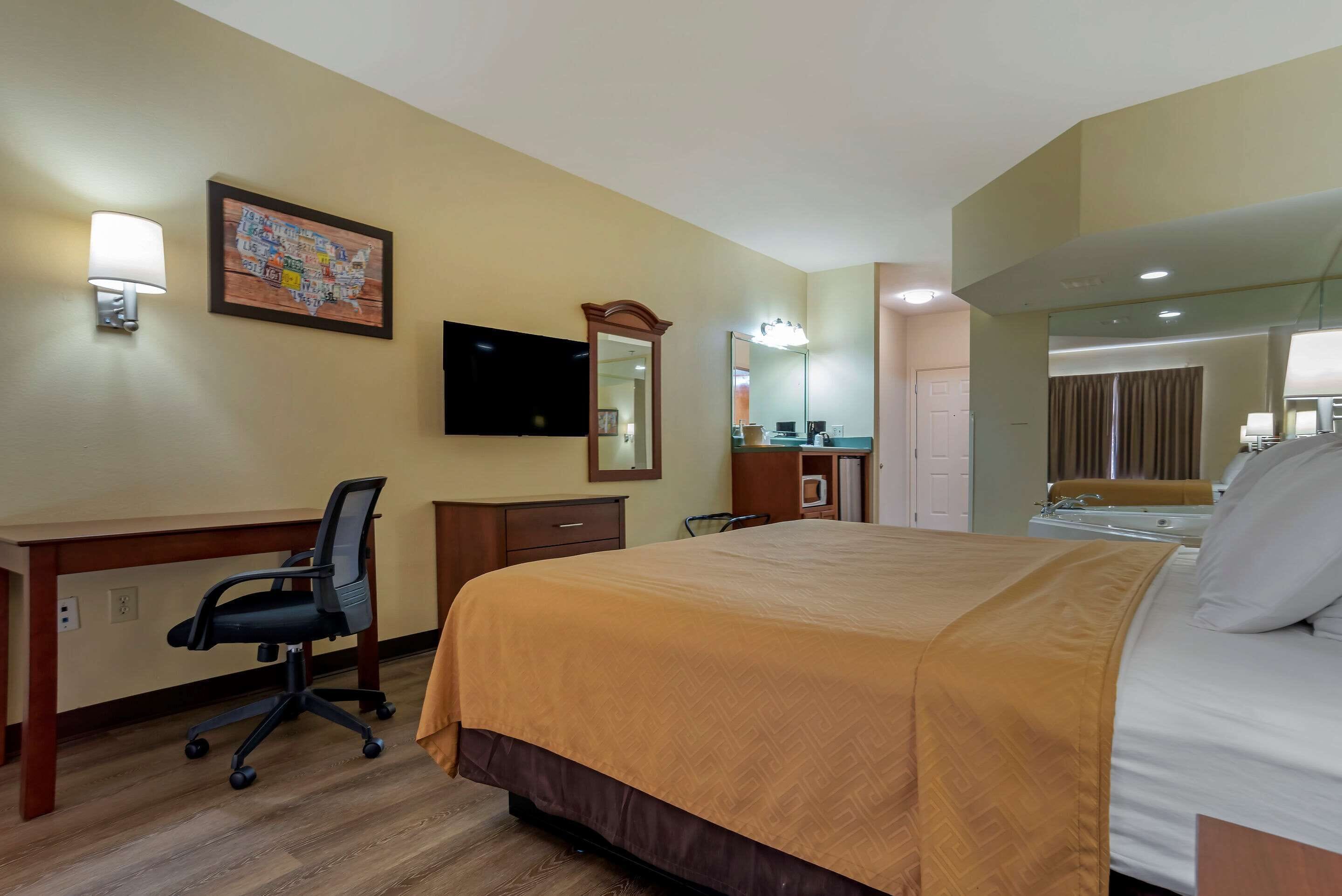 A hotel room with a bed, desk, chair, and a television on the wall.