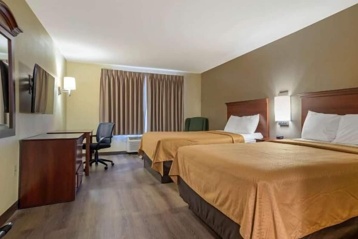 A hotel room with two beds, a desk, a chair, and a window with curtains.