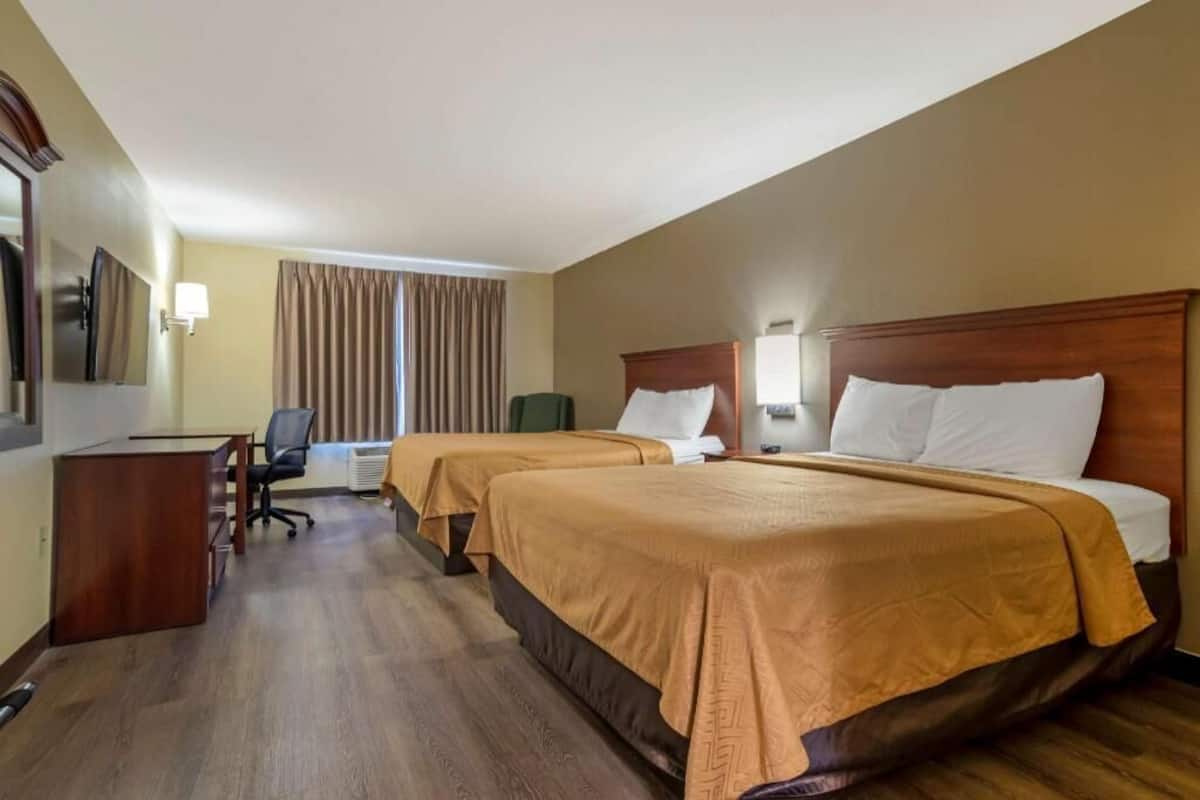 A hotel room with two beds, a desk, a chair, a mirror, and a window with curtains.