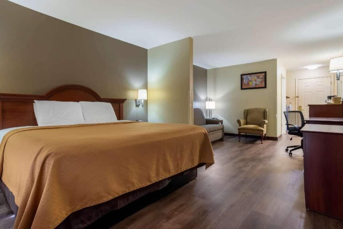 A hotel room with a bed, a desk, a chair, and a lamp.