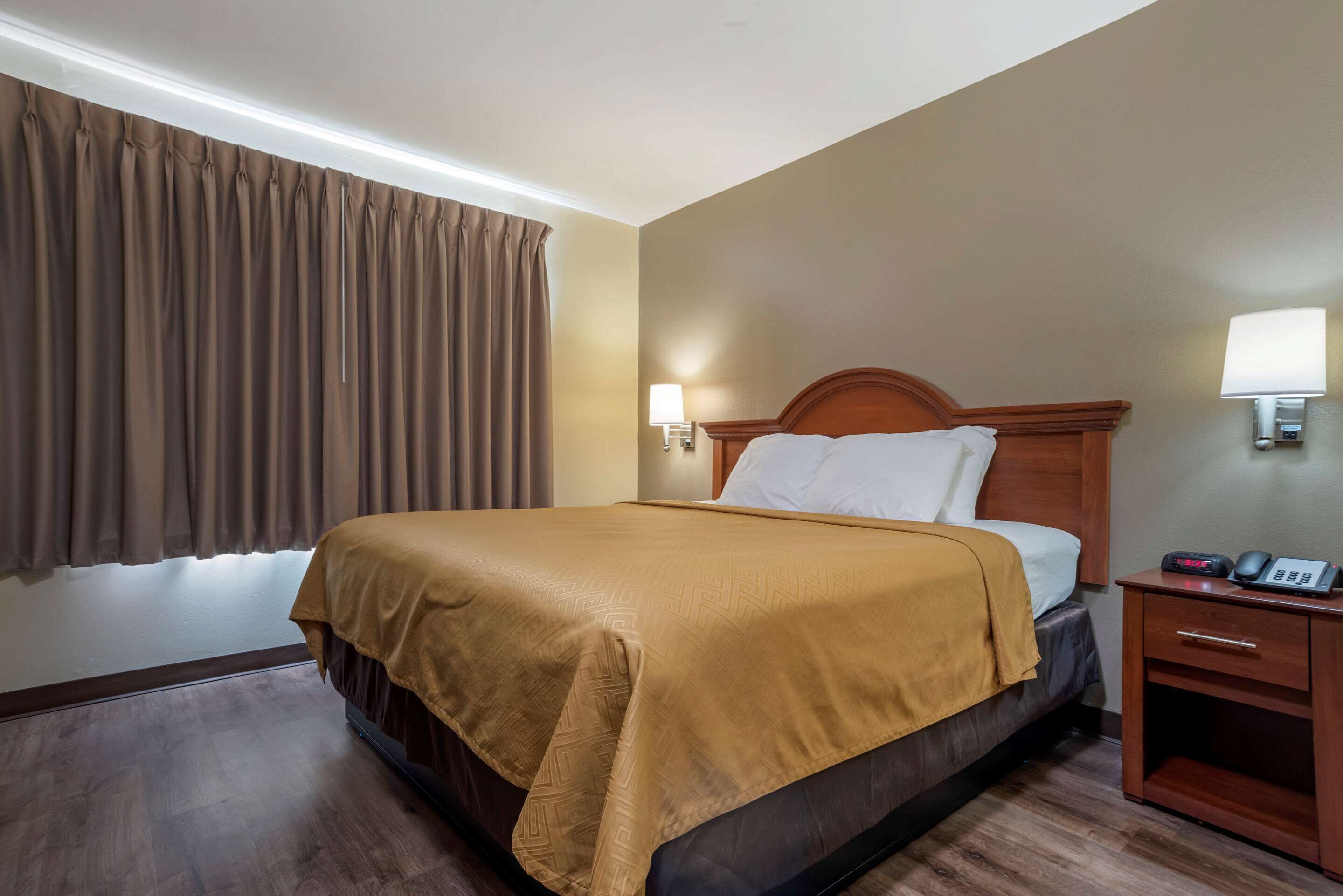 A hotel room with a bed, a nightstand, a lamp, and a window with curtains.