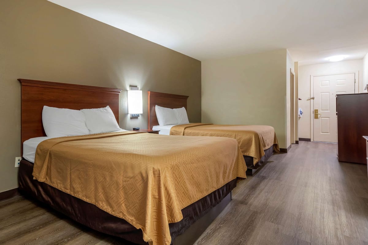 A hotel room with two beds, wooden headboards, and a nightstand with a lamp.