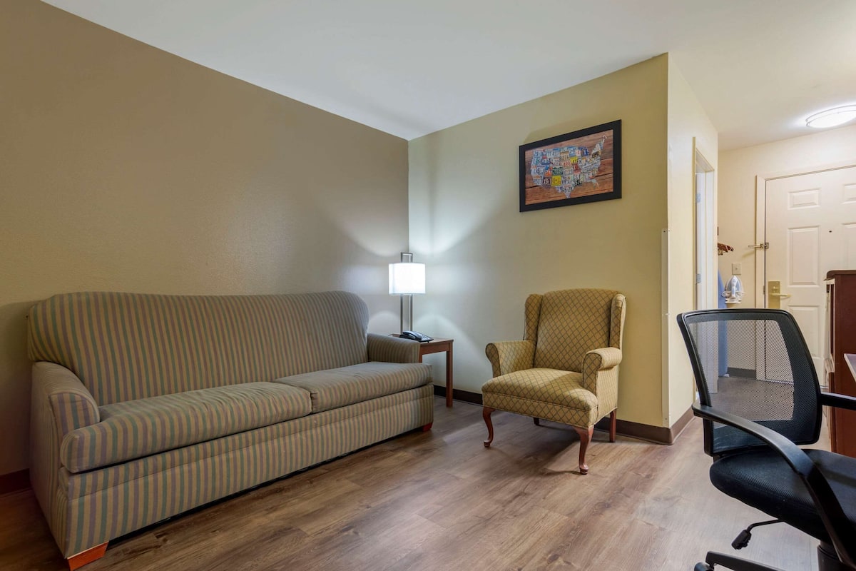 A living room with a striped sofa, a patterned armchair, a desk with a lamp, and a framed map on the wall.