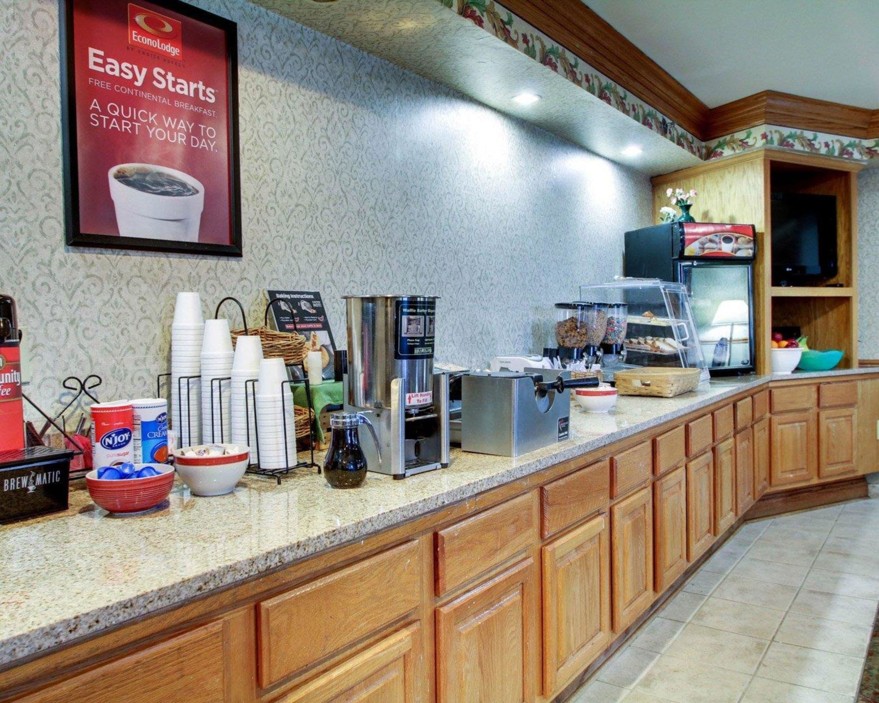 A breakfast bar with coffee machines, a waffle maker, and a variety of condiments.