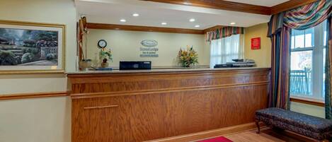 Un espace d’accueil avec un comptoir de réception en bois, une horloge, un ordinateur Dell et un tapis rouge orné du logo EconoLodge.