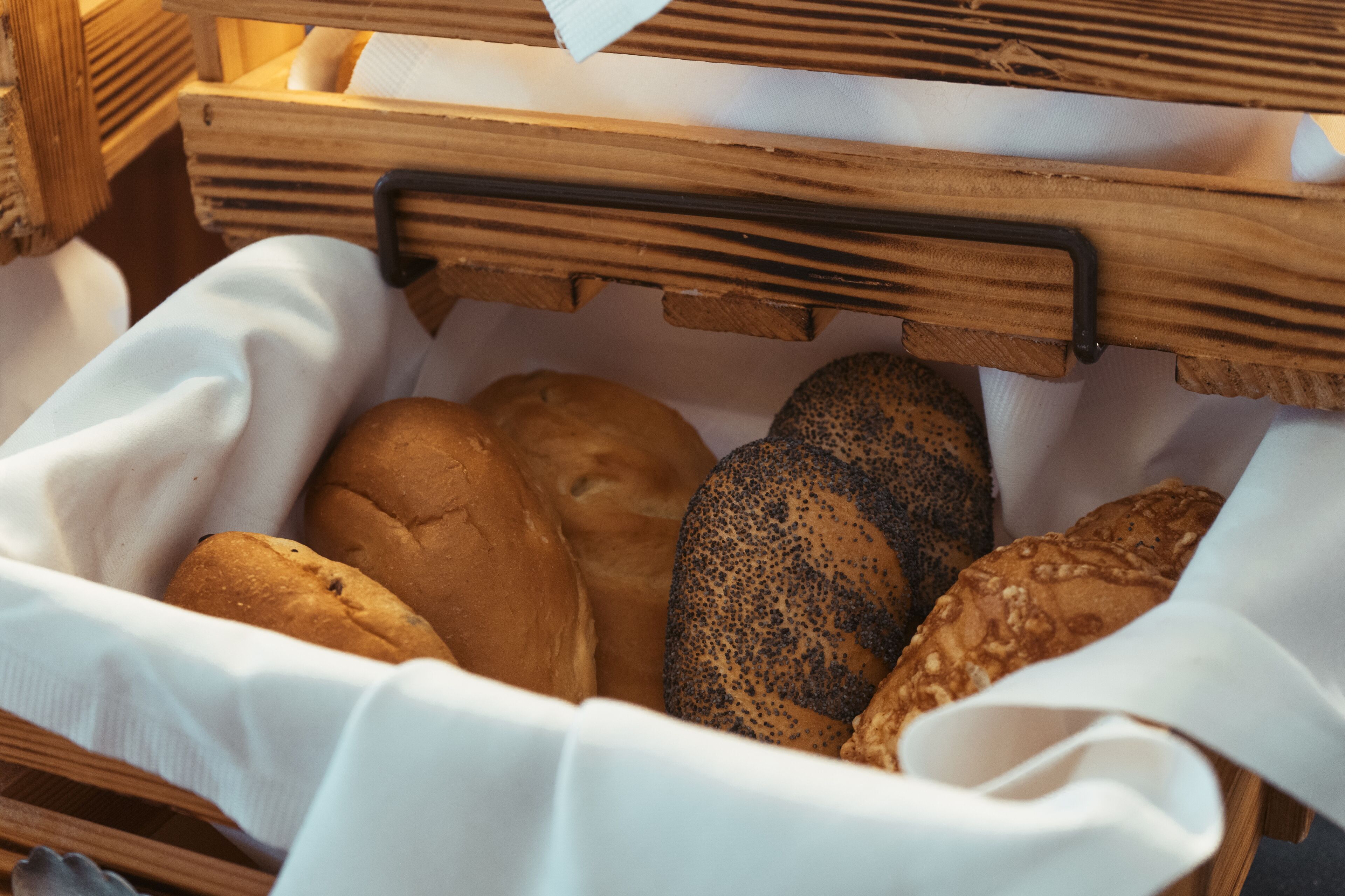 Ein Weidenkorb mit verschiedenen Brotsorten, darunter ein Mohnbrötchen, ein einfaches Brötchen und ein Körnerbrötchen.