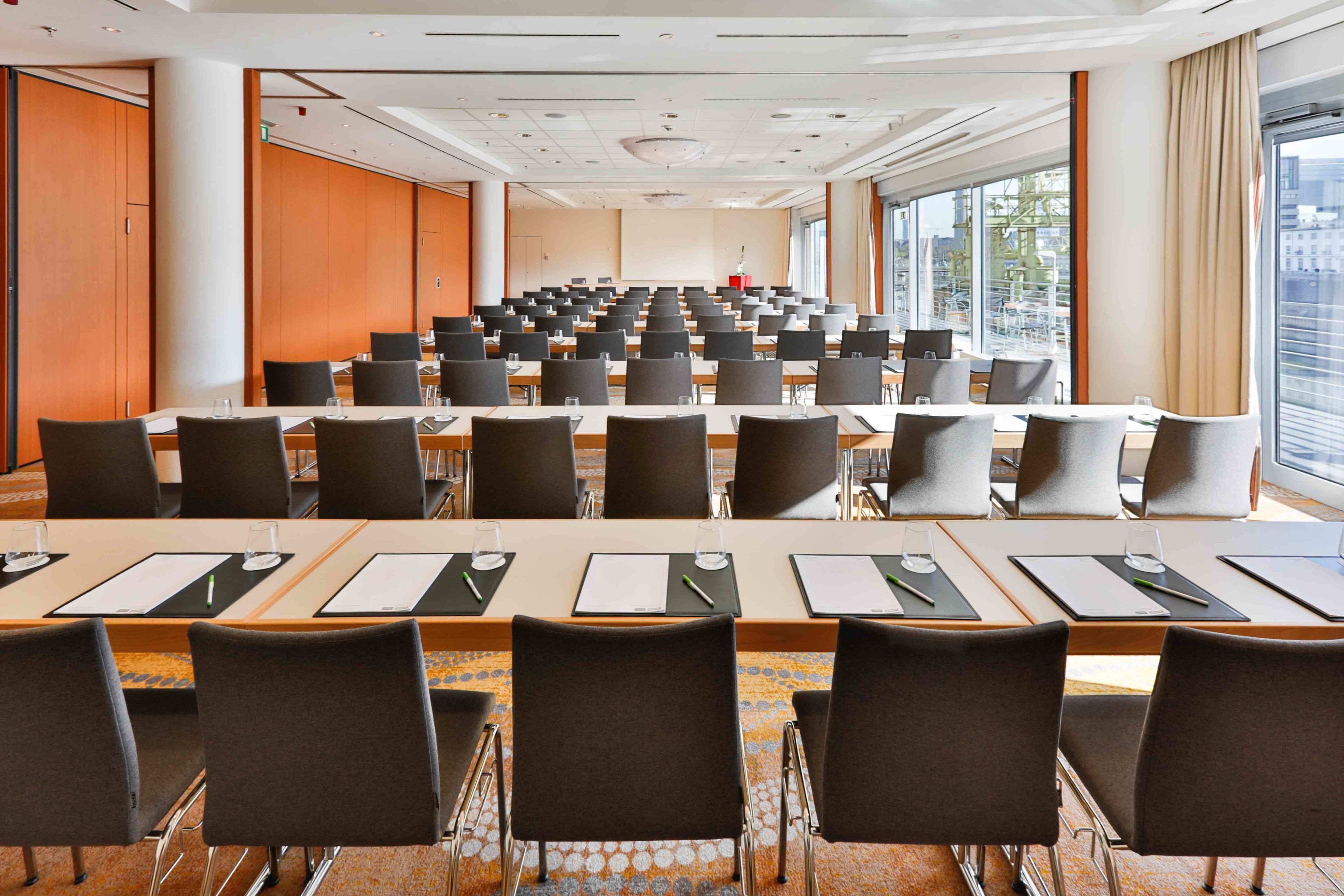 Une salle de conférence dotée de plusieurs tables et chaises, de grandes fenêtres et offrant une vue sur la ville.
