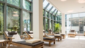 Un espace spa doté de chaises longues en bois, de grandes fenêtres et de plantes d’intérieur.