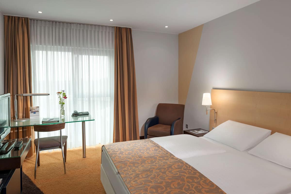 Ein Hotelzimmer mit einem Bett, einem Schreibtisch mit Stuhl, einem Fernseher und einer Lampe.