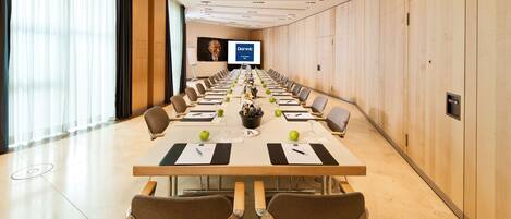 A conference room with a long table, chairs, and a screen at the front.