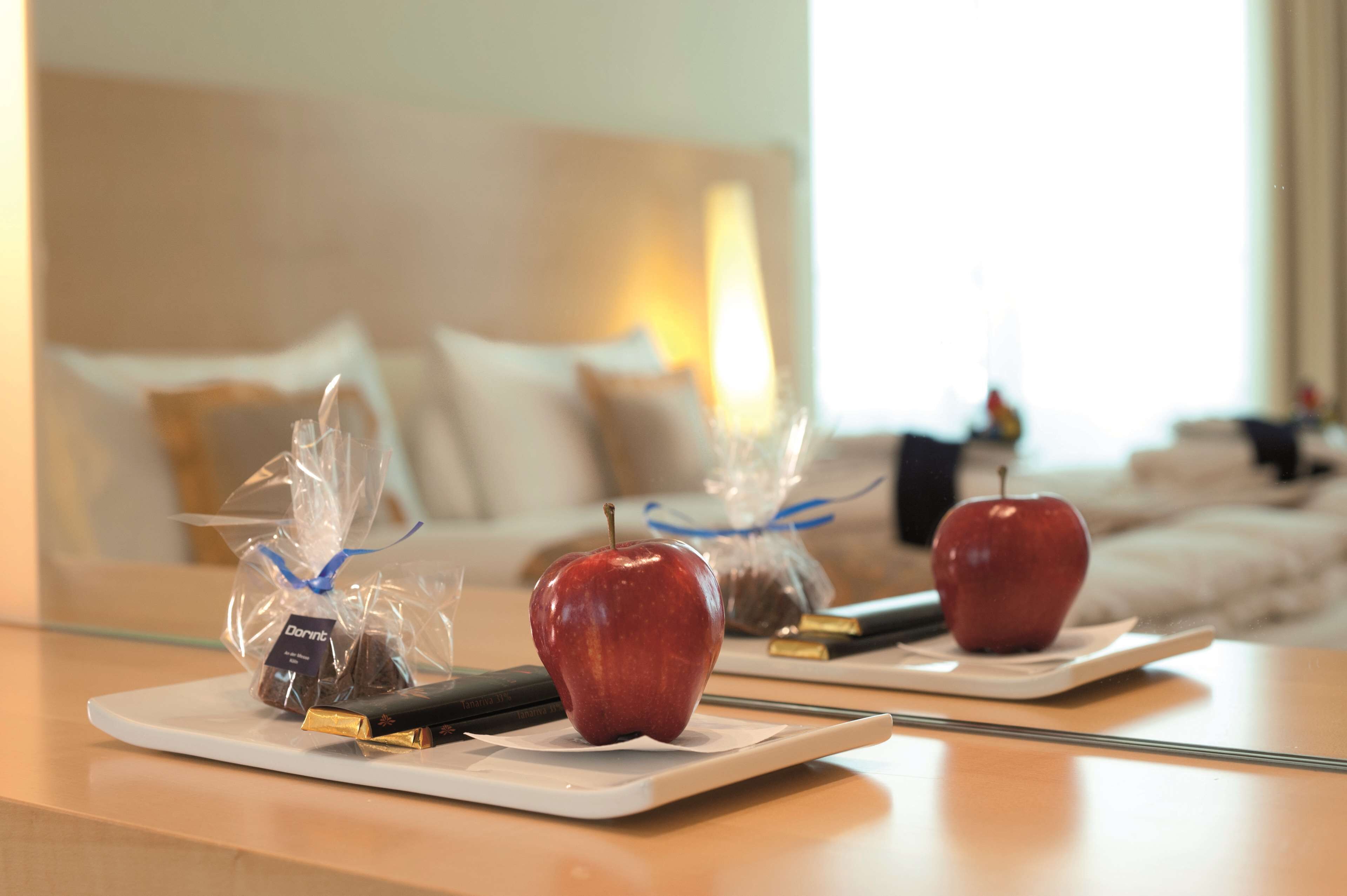 A hotel room with a dining table set with two apples and a chocolate bar, a remote control, and a book.
