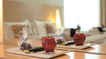 A hotel room with a dining table set with two apples and a chocolate bar, a remote control, and a book.