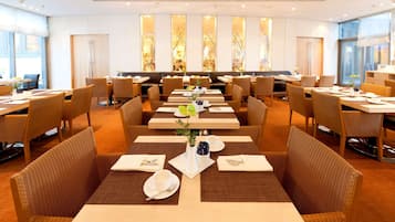 Un'area ristorazione di un hotel con diversi tavoli e sedie, disposti in un ambiente ampio.