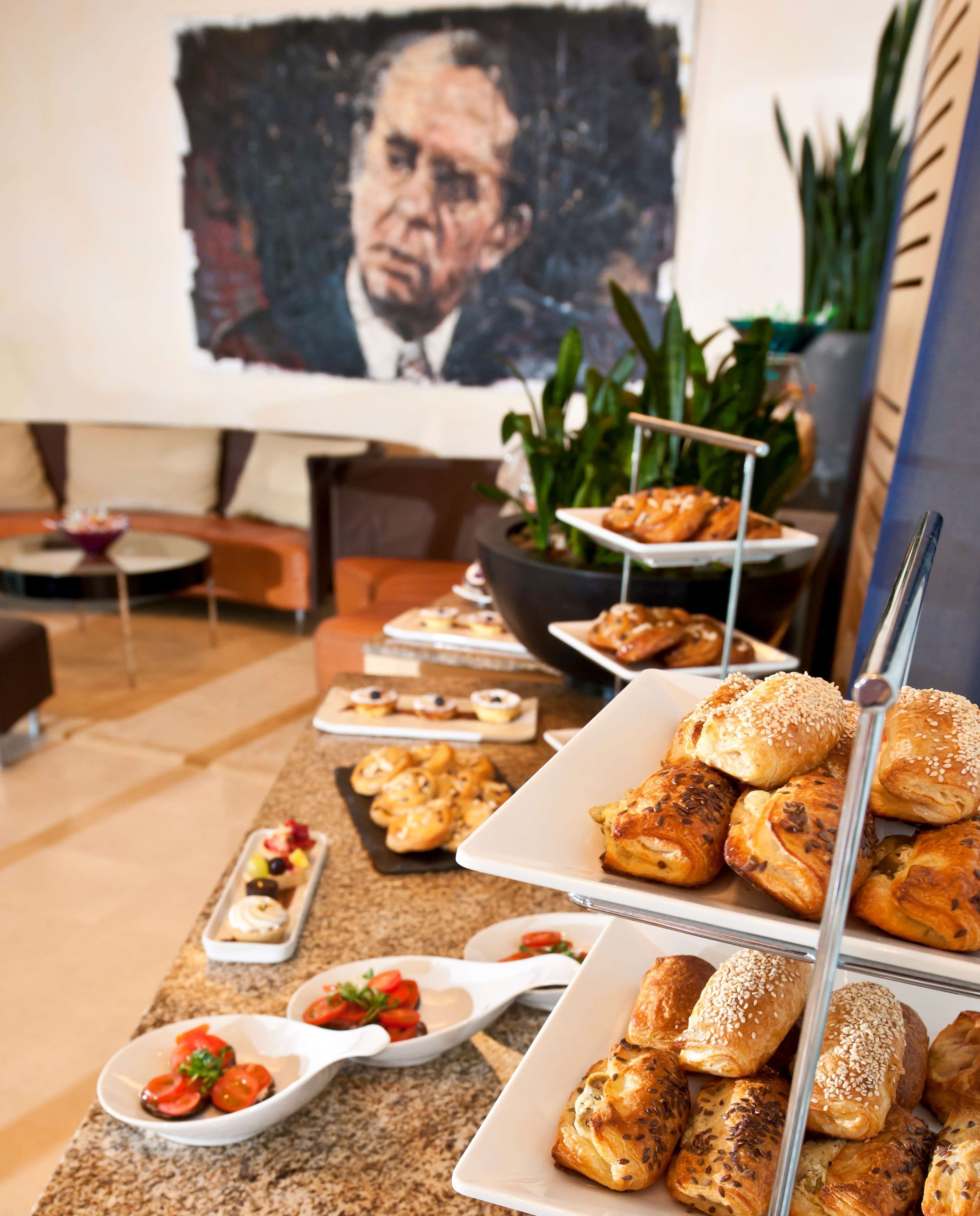 Una mesa de bufé con diversos pasteles y postres, un cuadro grande en la pared y una planta en maceta.