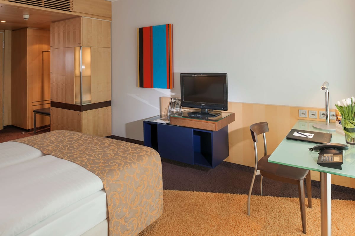 Ein Hotelzimmer mit Bett, Schreibtisch mit Computer, Stuhl und einem kleinen Tisch mit Blumenvase.