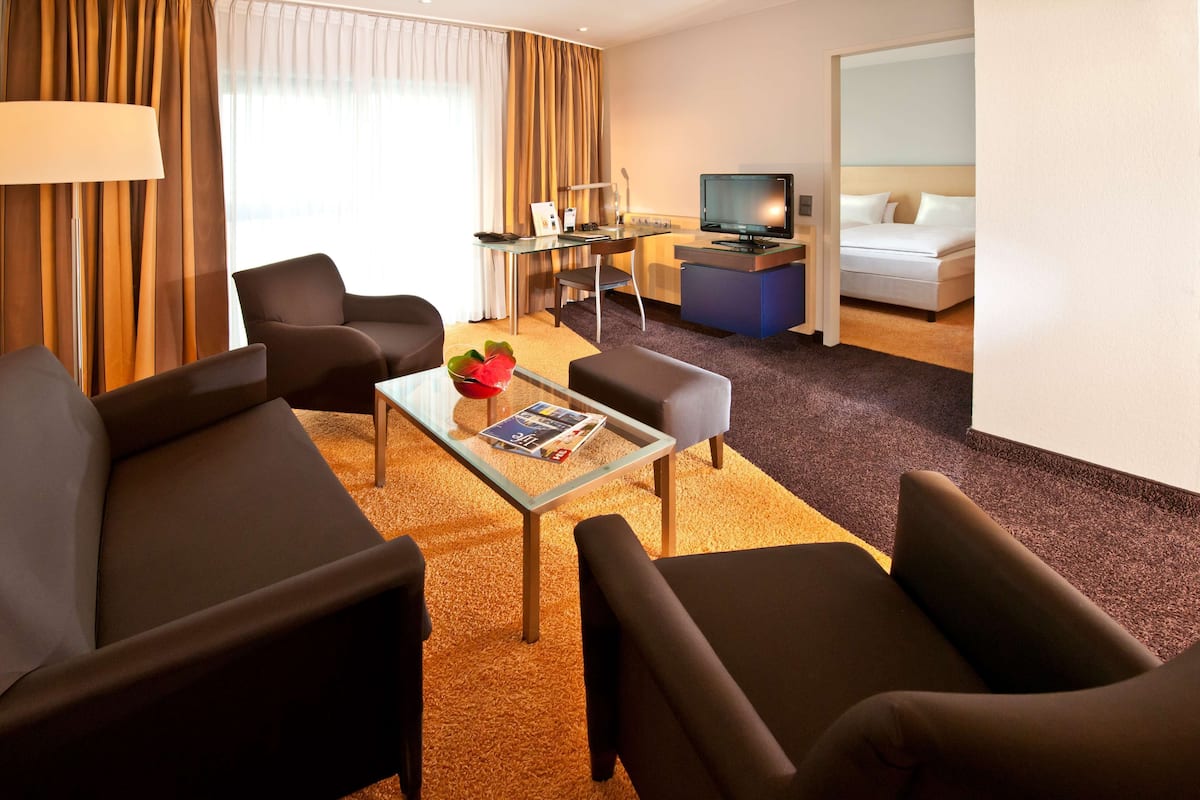 Ein Hotelzimmer mit einer Couch, Sesseln, einem Couchtisch, einem Schreibtisch mit Computer, einem Fernseher und einem Bett.