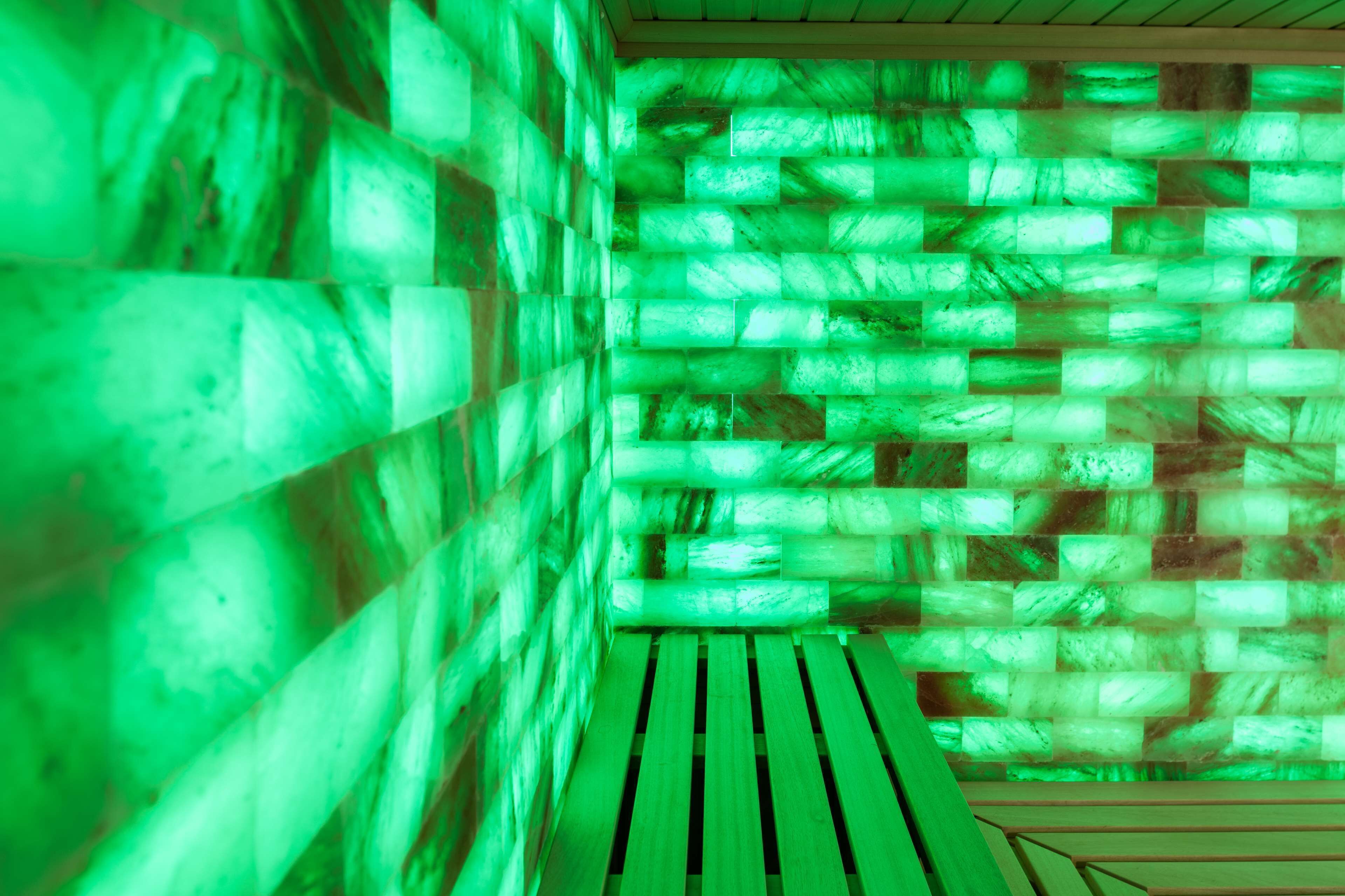 Une pièce avec un mur éclairé de lumière verte et un banc en bois.