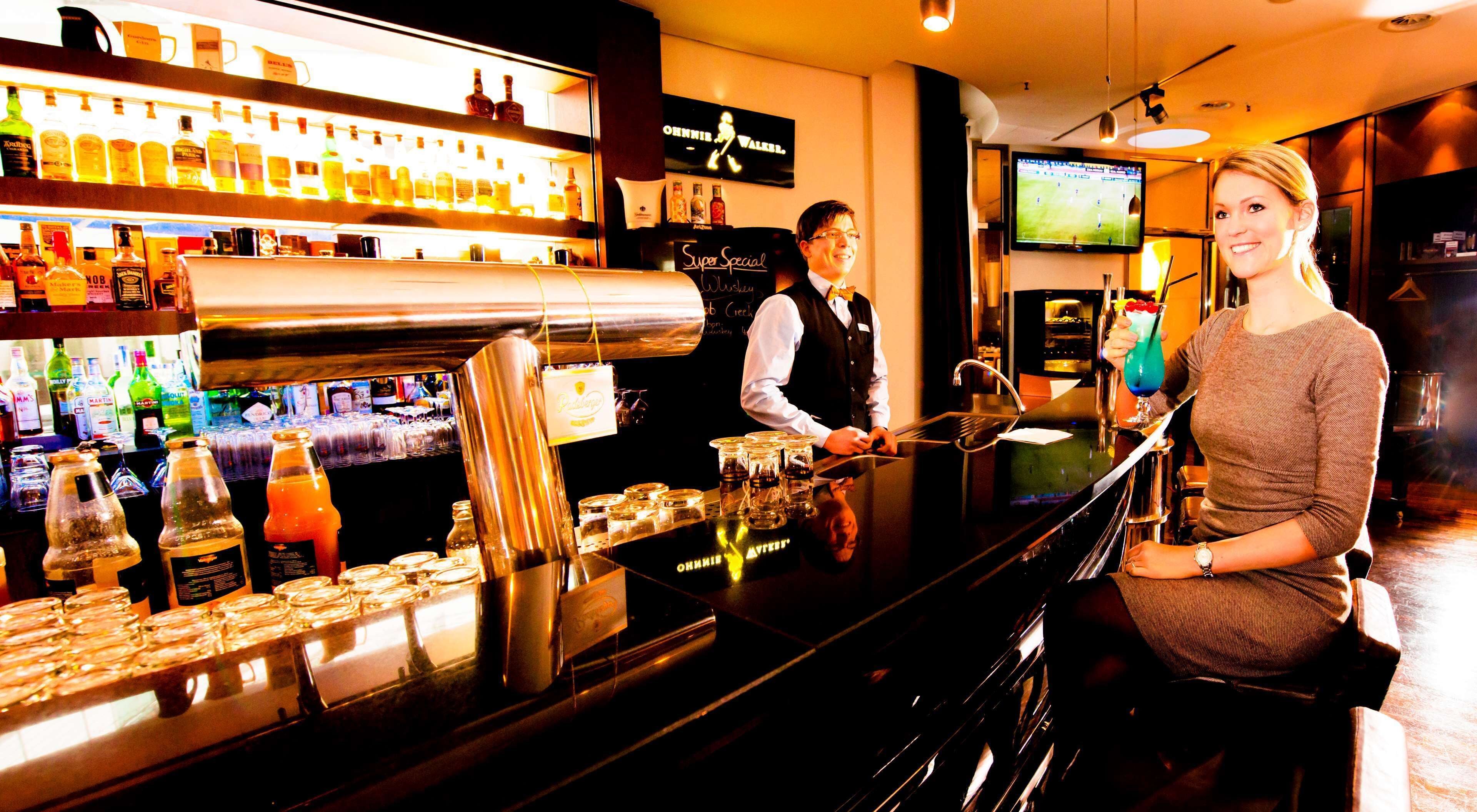 Eine Bar mit einem Barkeeper, einer sitzenden Frau und einem Fernsehbildschirm, der ein Sportspiel zeigt.