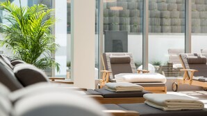 Un espace spa comprenant des fauteuils inclinables, une plante en pot et une vue sur un mur de pierre à travers de grandes fenêtres.