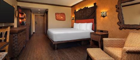 A hotel room with a large bed, a wooden dresser, a TV, a seating area with a patterned sofa, and a mirror on the wall.