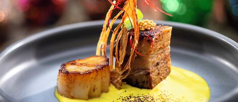 A plated dish with seared scallops and a piece of meat, garnished with a yellow sauce and black pepper.
