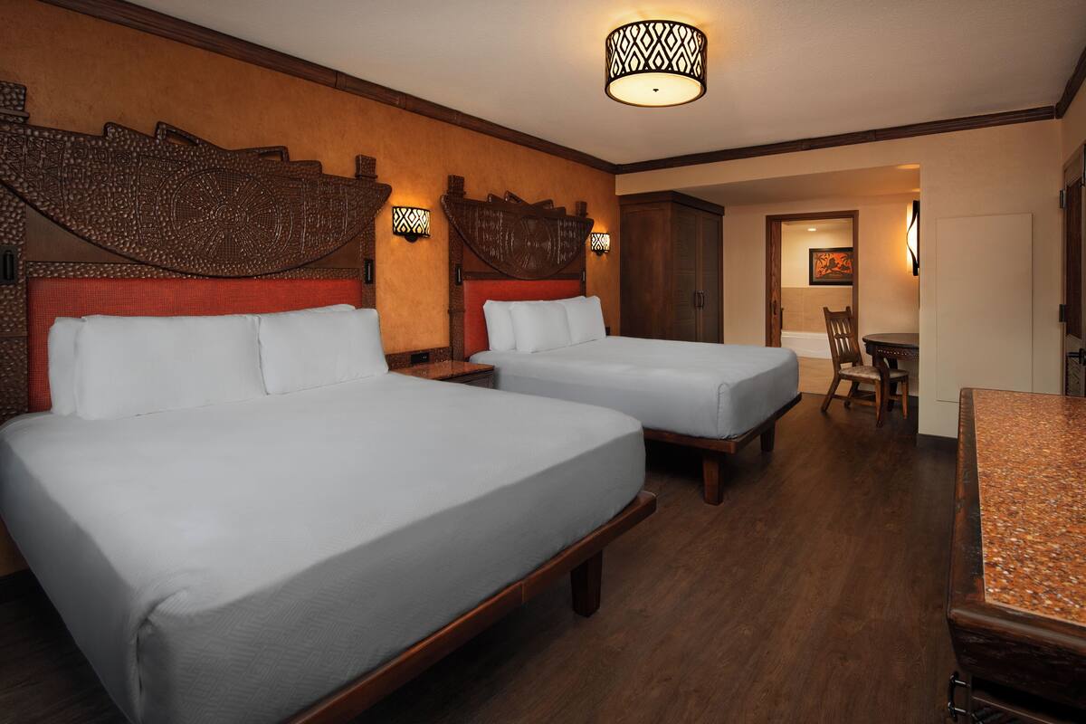 A hotel room with two beds, a wooden headboard, a small table, and a TV.