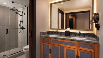 A modern bathroom with a glass-enclosed shower, two sinks, and wooden cabinets.