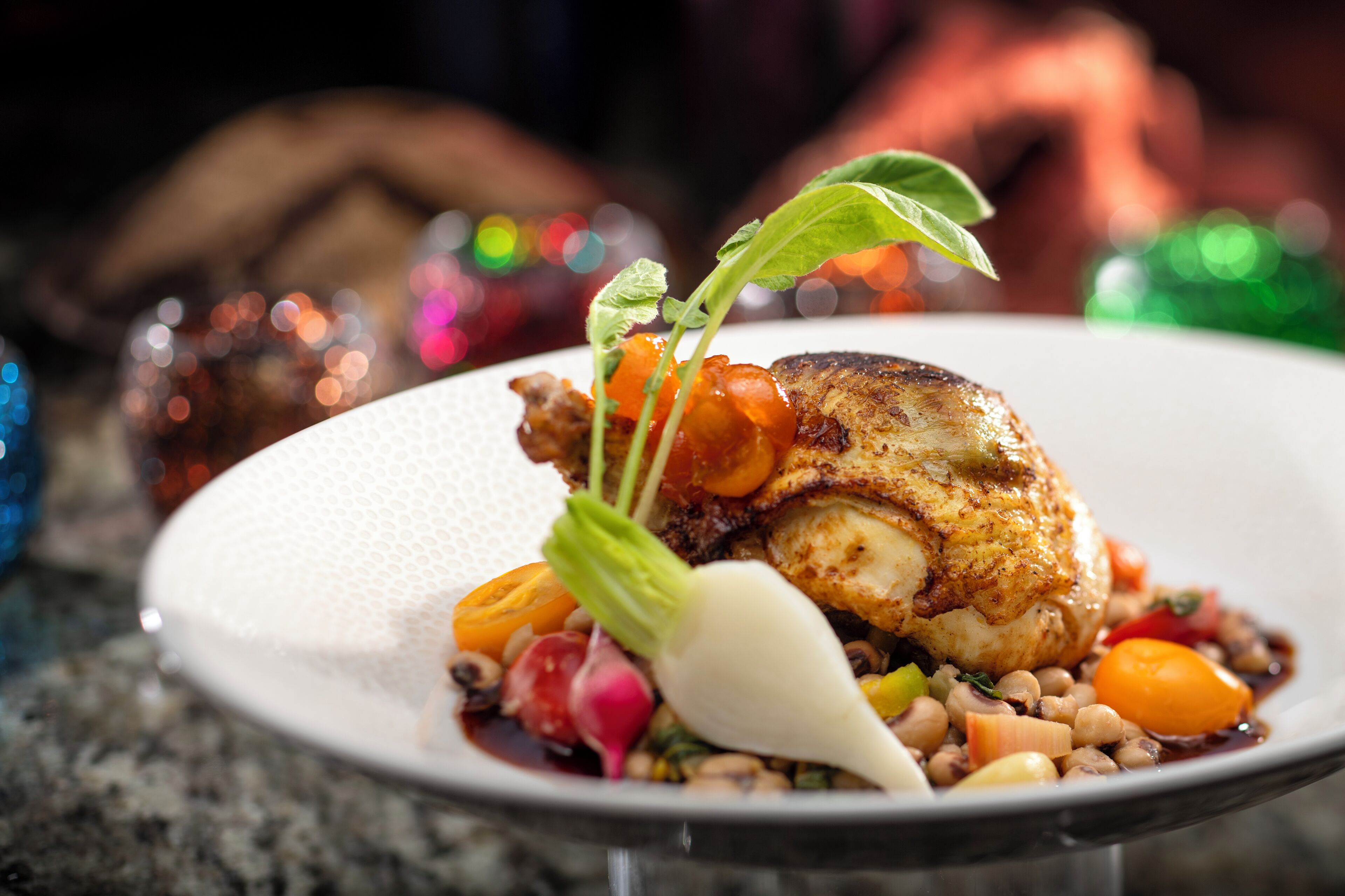 A plate of food with a roasted chicken, vegetables, and a decorative leaf.