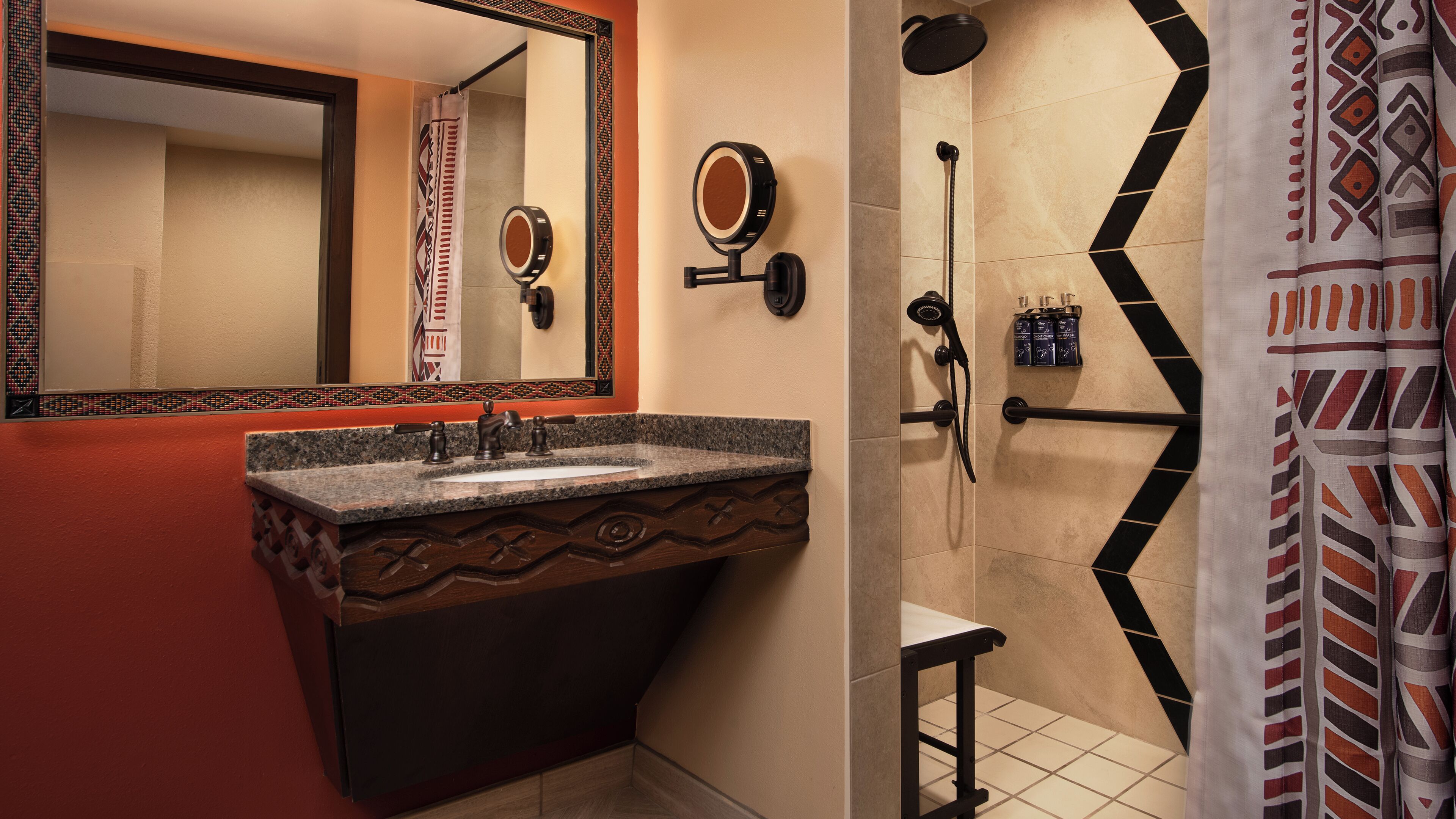 A bathroom with a granite sink, a mirror, a shower with a handheld showerhead, and a patterned shower curtain.
