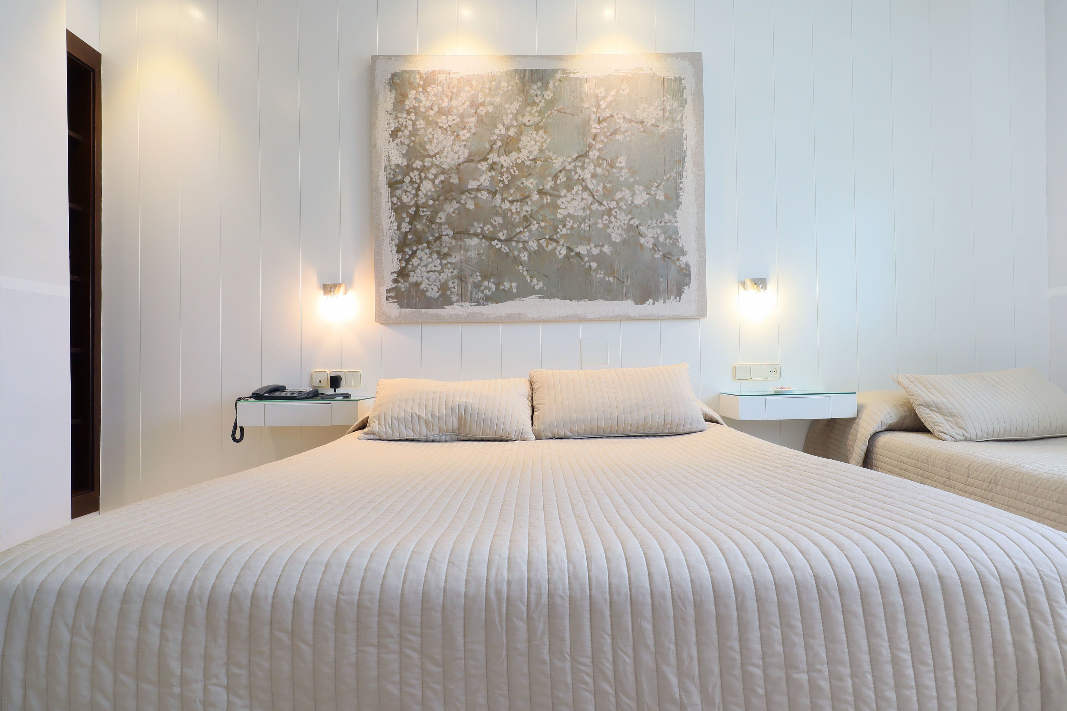 Un dormitorio con una cama grande, dos mesitas de noche, una obra de arte en la pared y una lámpara de noche.