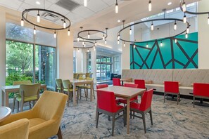 A modern dining area with round tables and chairs, a large window with a view of greenery, and a geometric wall design.
