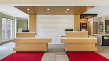 A hotel reception area with two counters, a patterned wall, and a red carpet.
