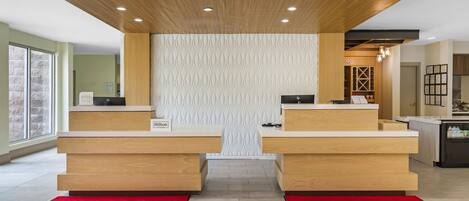 A hotel reception area with two counters, a patterned wall, and a red carpet.