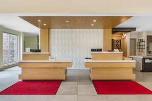 A hotel reception area with two counters, a patterned wall, and a red carpet.