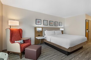 Una camera d'albergo con un letto, una sedia, un tavolino, un comodino e una lampada.