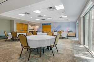 Un salón de conferencias con mesas redondas, sillas y un ventanal grande.