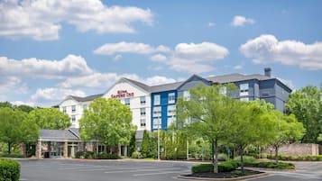 Un hotel de varios pisos con un llamativo letrero de 'Hilton Garden Inn', un estacionamiento y zonas verdes circundantes.