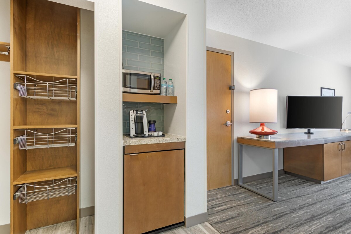A hotel room with a kitchenette, a microwave, a coffee maker, and a television.