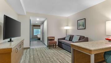 A hotel room with a television, a sofa, a desk, and a lamp.
