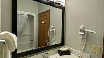Un baño con lavamanos, espejo, secador de pelo y toallero.