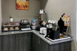 A breakfast bar with various food items, a waffle maker, and a coffee machine.