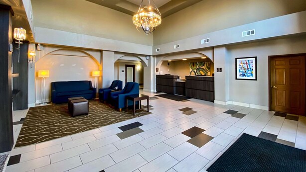 A spacious living area with a blue sofa, two armchairs, a coffee table, and a chandelier. - Comfort Inn Owasso - Tulsa (Owasso)