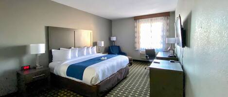 A hotel room with a large bed, a desk, a chair, and a TV.