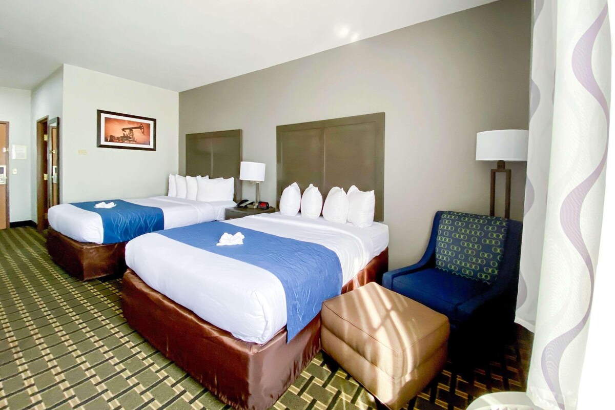 A hotel room with two beds, a sofa, a chair, and a lamp.